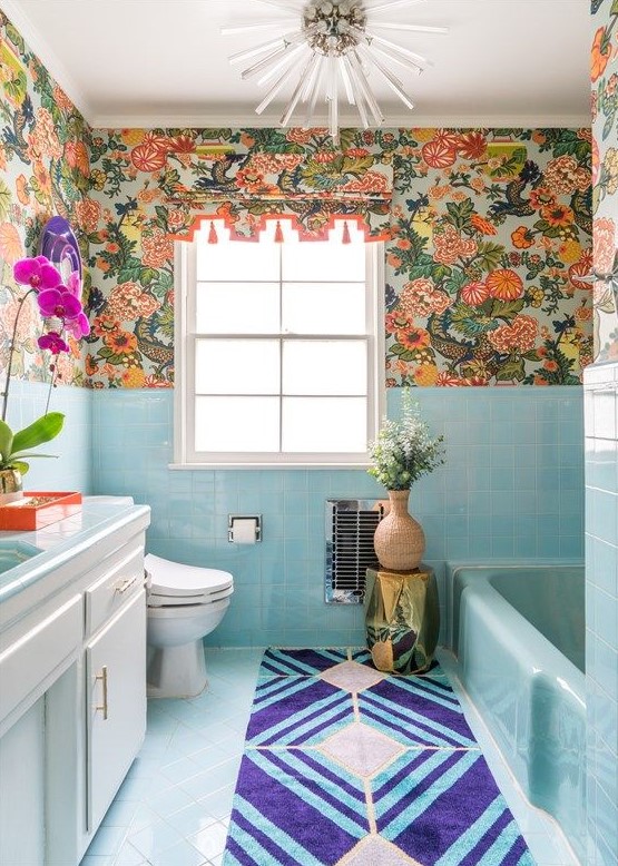 a bright maximalist bathroom with blue tiles and a bathtub, bright florla wallpaper, bold blooms and a sunbrust chandelier