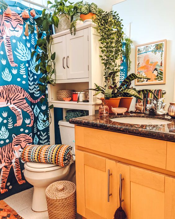 a bright maximalist bathroom with bold wallpaper, a yellow vanity with stone countertop, potted greenery, bold artwork and a cabinet for storage
