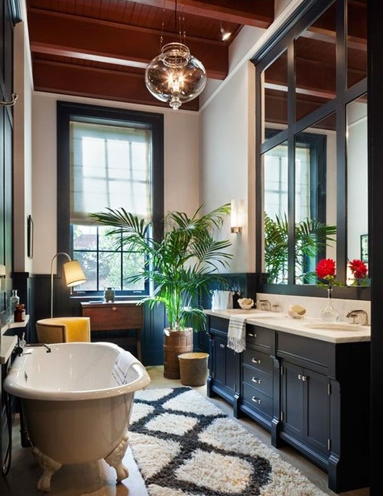 a catchy eclectic bathroom with navy paneling and a vanity, a large mirror with frames, a clawfoot tub and a statement plant
