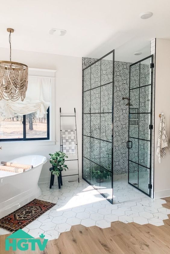 a catchy eclectic bathroom with printed tile in the shower, a tub by the window, a tile and laminate floor and a bead chandelier