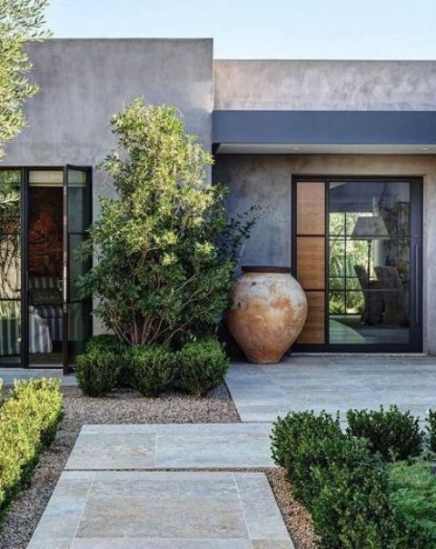 a chic and edgy modern front yard with greenery and trees, with an oversized shabby chic planter and stone garden paths