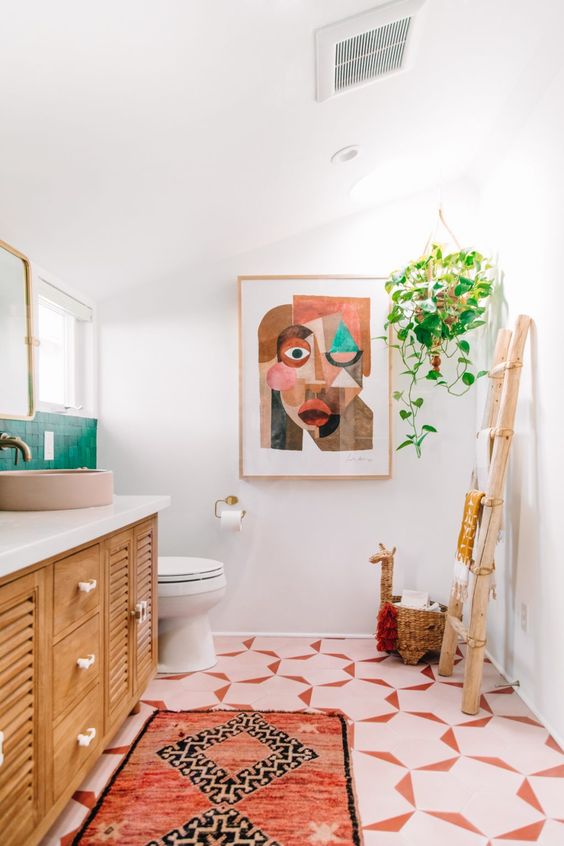 a colorful eclectic bathroom with a pink tile floor, a stained vanity, pink sinks, a bold artwork, some greenery and green tile on the wall
