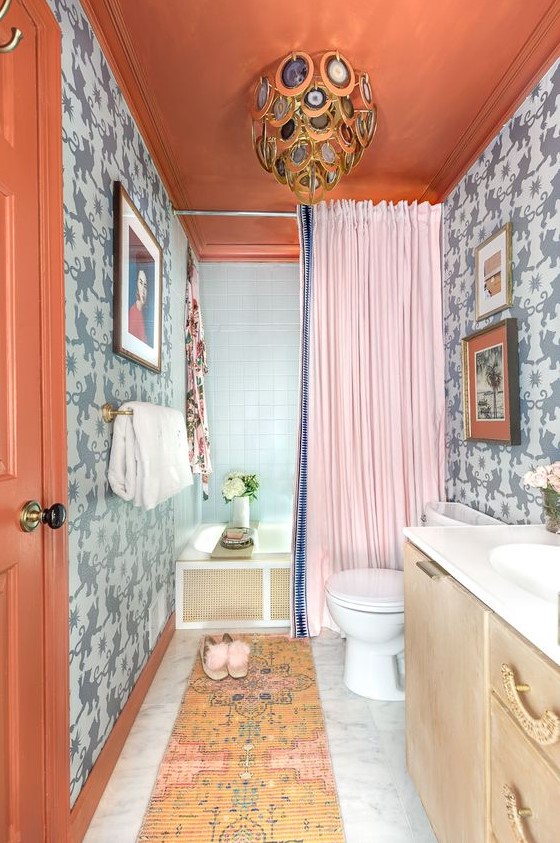 a colorful maximalist bathroom with grey printed walls, a rust ceiling and a door, a bold rug, a creative agate chandelier and a pink curtain