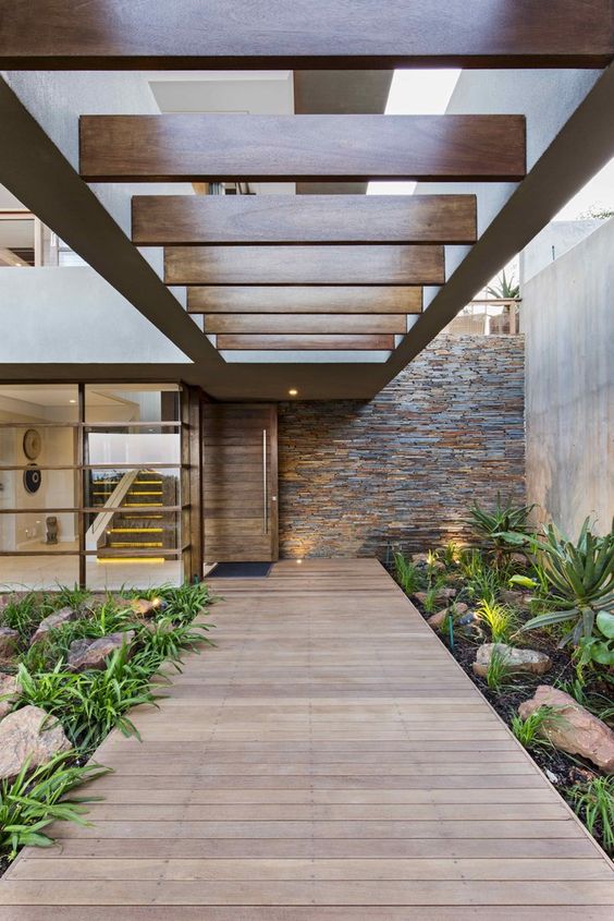 a cool modern front yard with greenery and large rocks plus a wooden deck and some lights around is a lovely space
