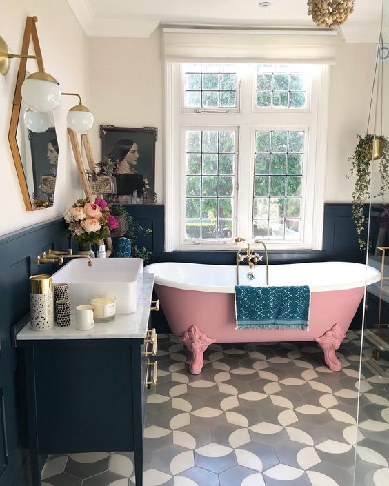 a gorgeous pink roll top clawfoot bathtub and statement tiles on the floor, all pulled together with a navy decor and statement lighting