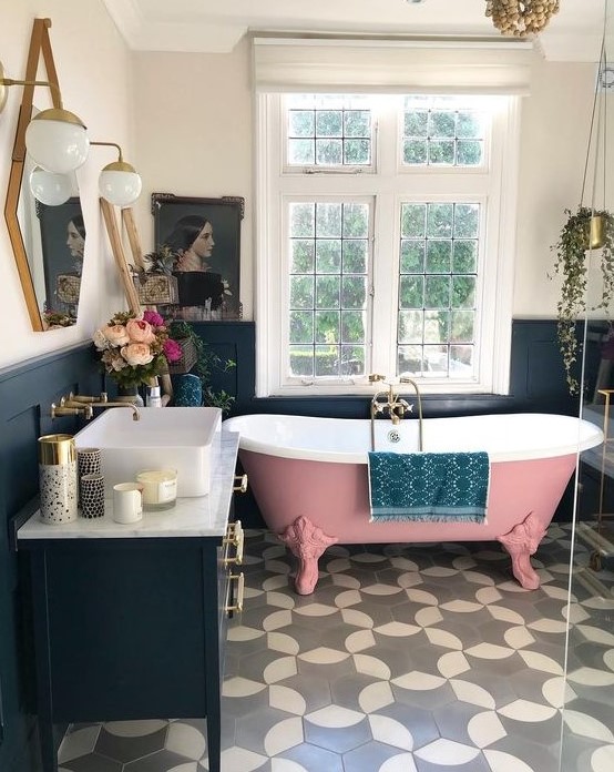 a gorgeous pink roll top clawfoot bathtub and statement tiles on the floor, all pulled together with a navy decor and statement lighting