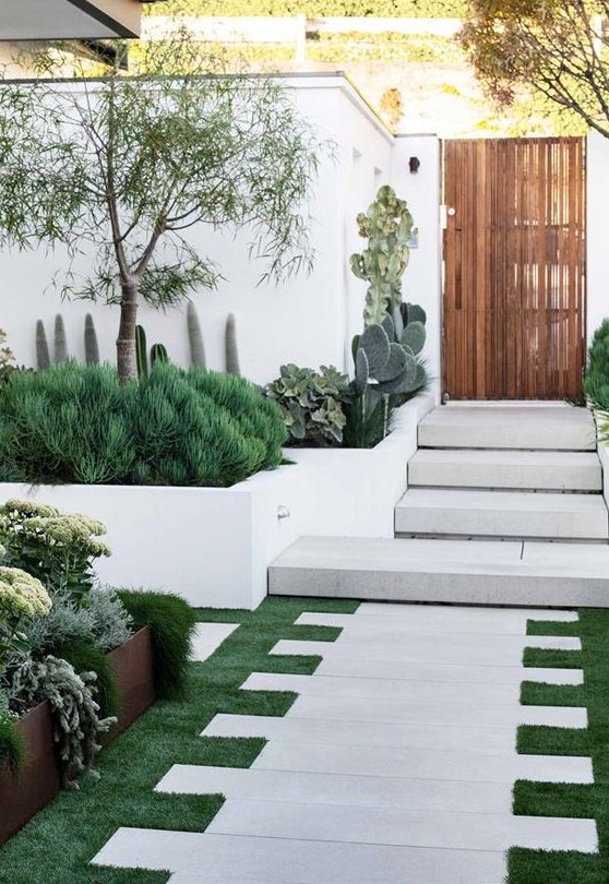 a jaw-dropping front yard with grass and stone tiles, with greenery, cacti, trees and succulents is a very welcoming space