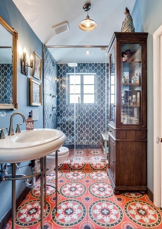 a maximalist bathroom with blue walls and blue tiles, a red mosaic tile floor, a stained storage cabinet and a smal gallery wall