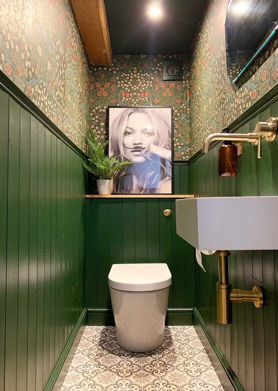 a maximalist bathroom with floral wallpaper, green paneling, an artwork and a statement artwork and brass touches