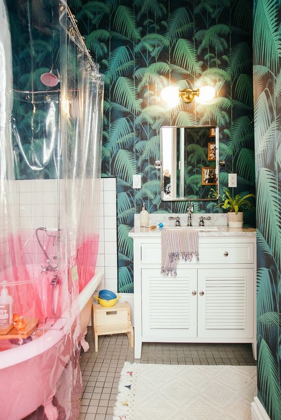a maximalist bathroom with tropical leaf walls, a pink bathtub, a color block curtain, white furniture and neutral textiles