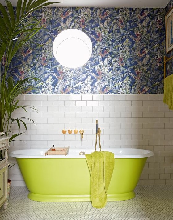 a maximalist bathroom with white subway tiles, dark tropical leaf wallpaper, a neon green bathtub and towels, a statement plant