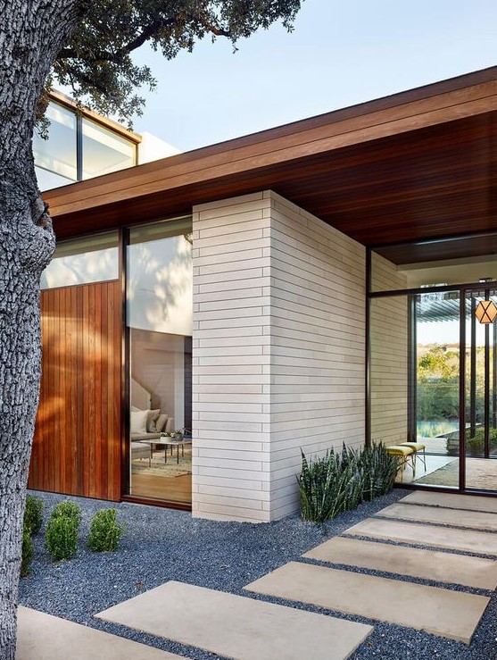 a modern and very laconic front yard with gravel, stone tiles, greenery, succulents plus a living tree is a very chic and stylish space