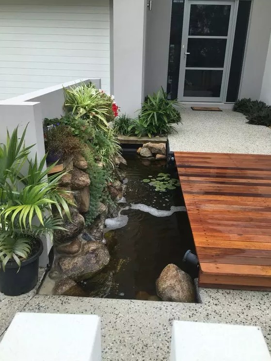 a modern entrance with a stained path, a water feature with rocks and greenery plus spotlights is great and chic