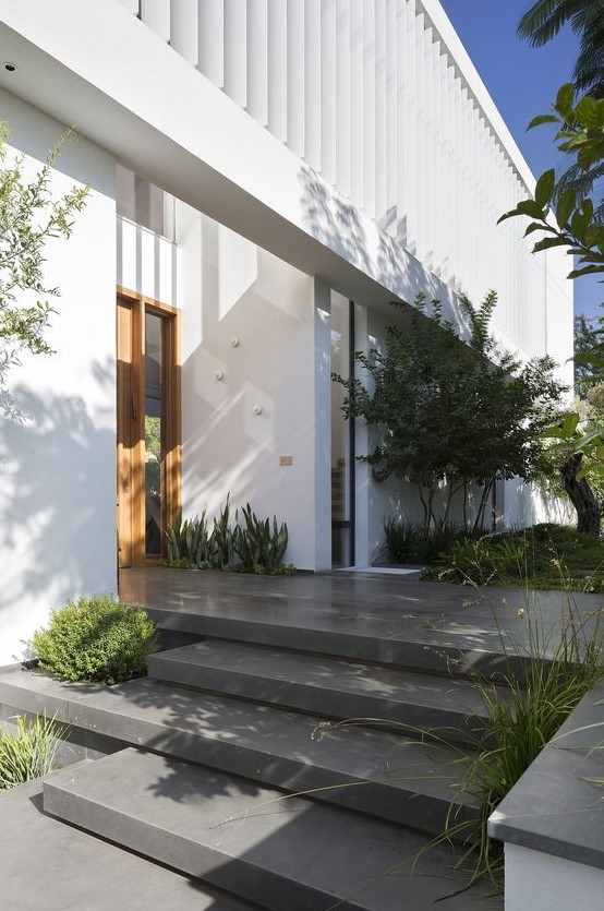 a modern front yard clad with stone tiles and with some greenery growing in the steps and with trees and succulents growing around the house