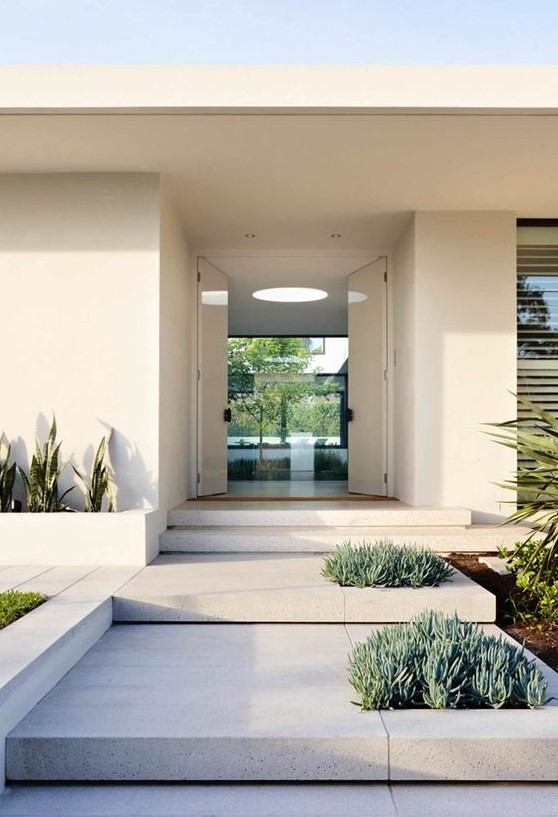 a modern front yard clad with stone tiles and with succulents and cacti growing right in the tables and in built-in planters is very sleek and elegant