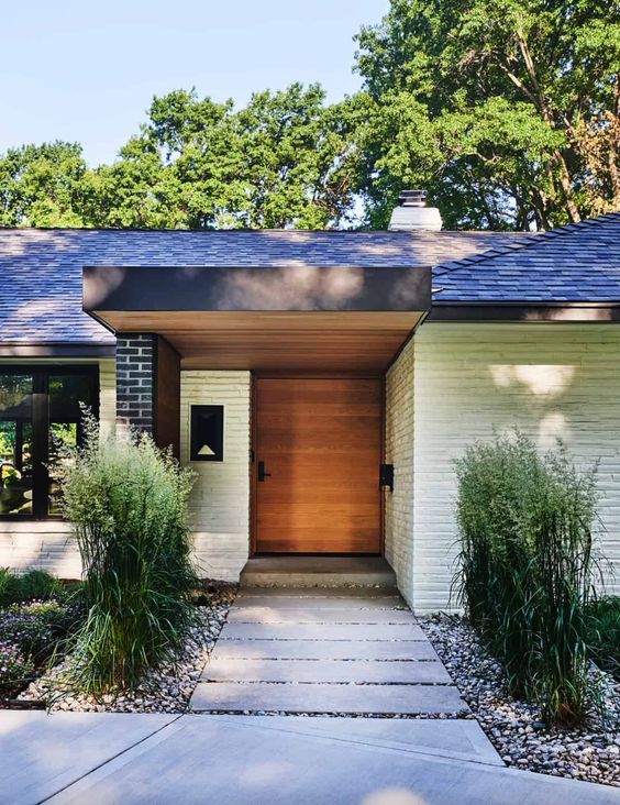 a modern front yard with a stone path and gravel, some greenery, blooms and shrubs is a cool and chic space