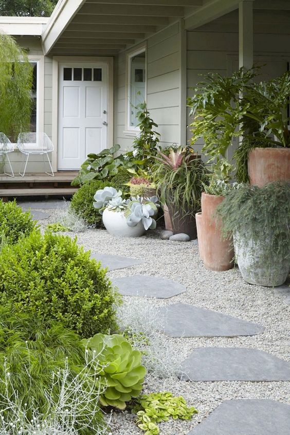 a modern front yard with gravel and rock paths, greenery and succulents, greenery and succulents in oversized plants is a stylish space