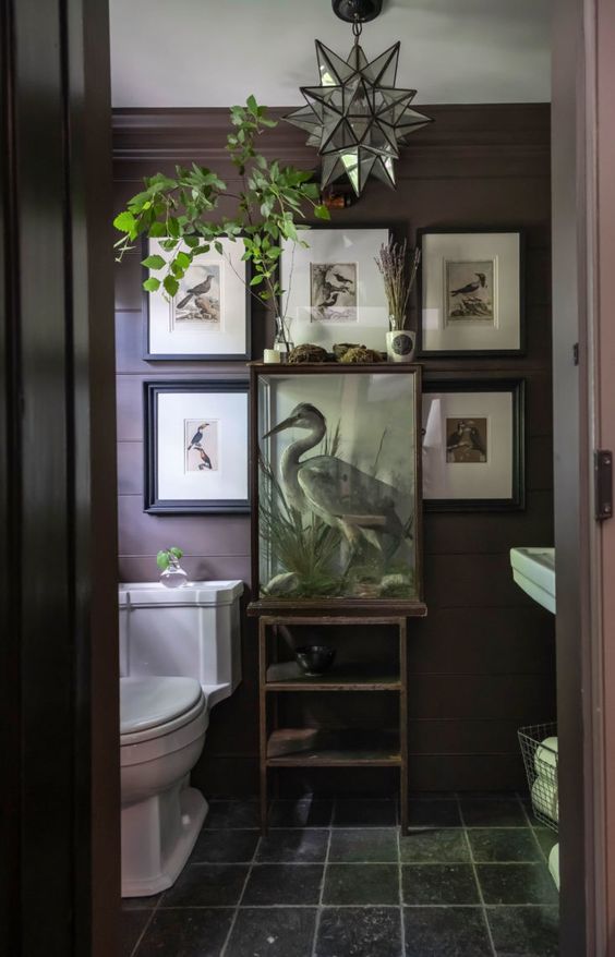 a moody eclectic powder room with brown walls, white appliances, a catchy gallery wall and some greenery