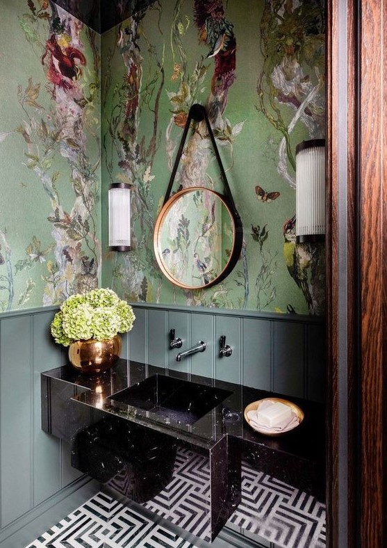 a refined maximalist bathroom with green flora and fauna wallpaper, a black stone vanity, a mosaic tile floor and a round mirror