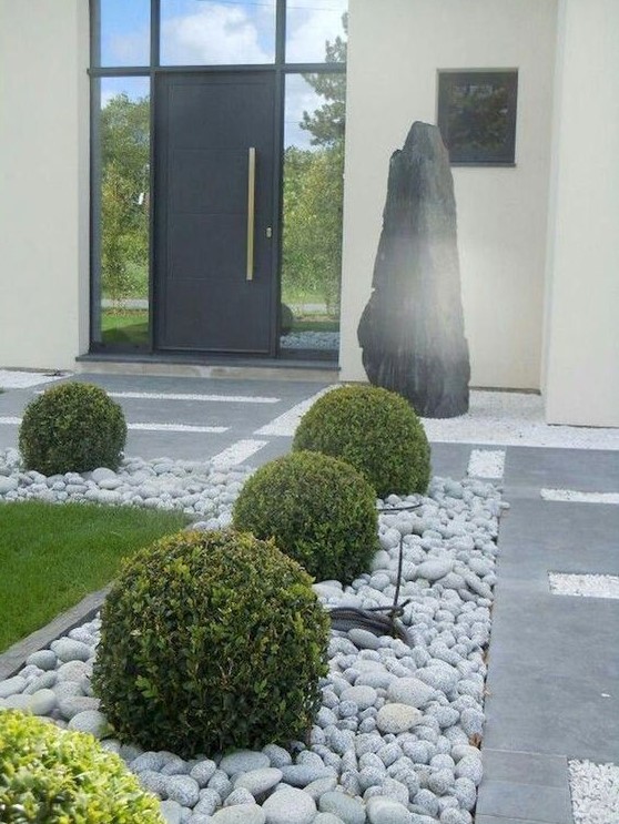 a refined modern front yard with stone tiles and rocks, with grass and elegant greenery balls looks chic and ultimate and inspires