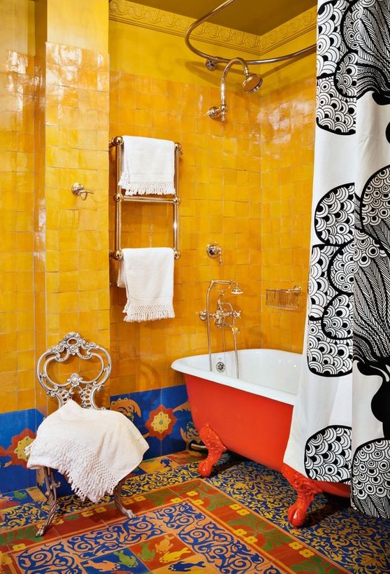 a super bold maximalist bathroom with bold yellow and blue tiles, colorful mosaic tiles on the floor, a red bathtub, a vintage chair