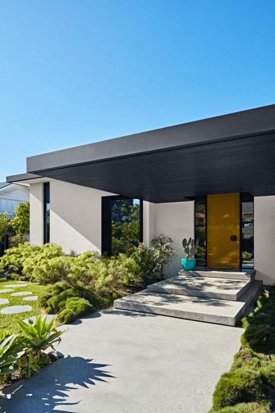 a super stylish modern front yard with greenery and shrubs, a large concrete path with steps and a potted cactus is very chic