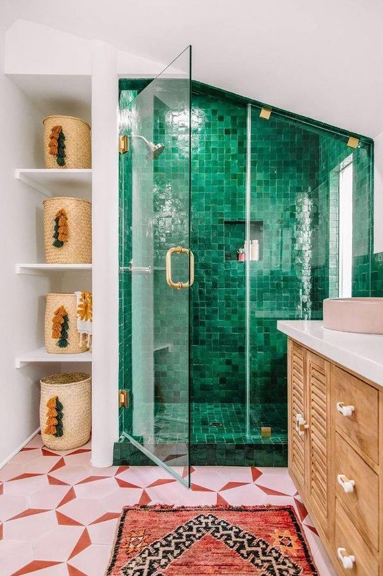 a vibrant maximalist bathroom with a pink and red tile floor, a green tile shower space, a red rug and baskets with tassels