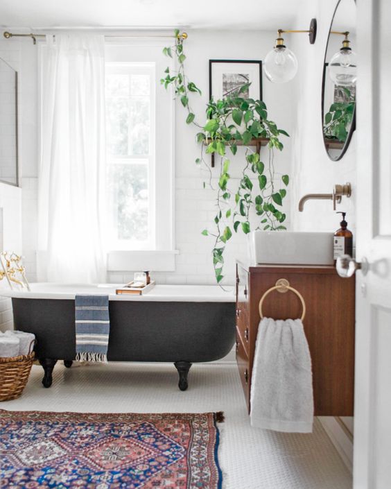 a vintage eclectic bathroom with a boho rug, a vintage black bathtub, potted greenery and a floatign vanity with a sink