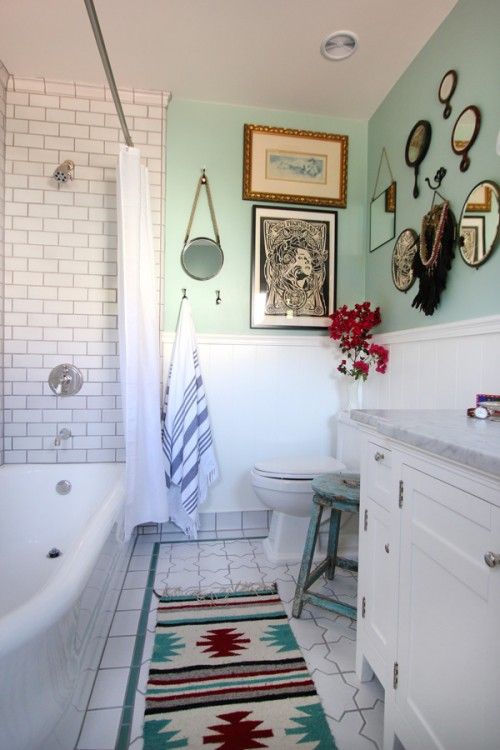 a vintage meets boho chic bathroom, with lots of mirrors and paintings, with a colorful rug and subway tiles