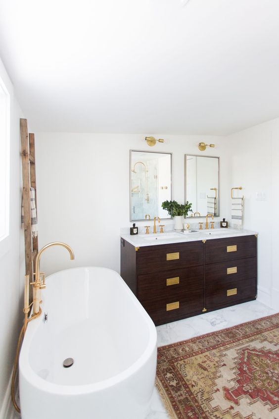 an art deco meets boho eclectic bathroom with lots of brass, boho rugs and a dark stained vanities