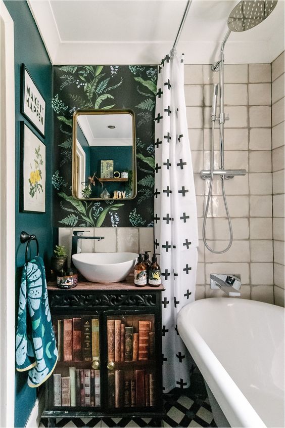 an eclectic bathroom with a dark green, botanical wallpaper and white tile wall, a vanity with books, bold textiles and a tub