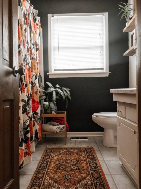an eclectic bathroom with black walls, white appliances, a bold shower curtain and a bright rug, potted greenery
