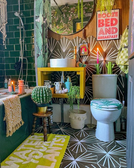 an eclectic bathroom with green and geometric tile, a yellow vanity with a sink, a bold rug, some artwork, potted plants and a round mirror