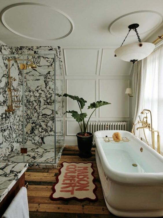 an eclectic bathroom with neutral paneling, a white marble shower space, a tub, a rug, a potted plant and a chandelier