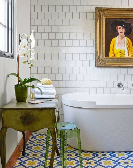 an eclectic bathroom with square and colorful tiles, an oval tub, a vintage vanity, a green acrylic stool and an artwork