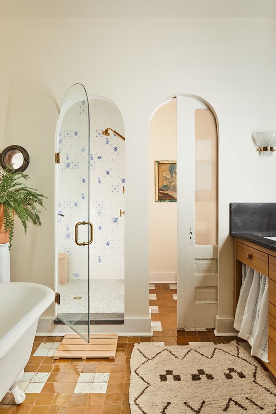 an eclectic neutral bathroom with arched doors, a white tub, a stained vanity, a printed rug and potted greenery