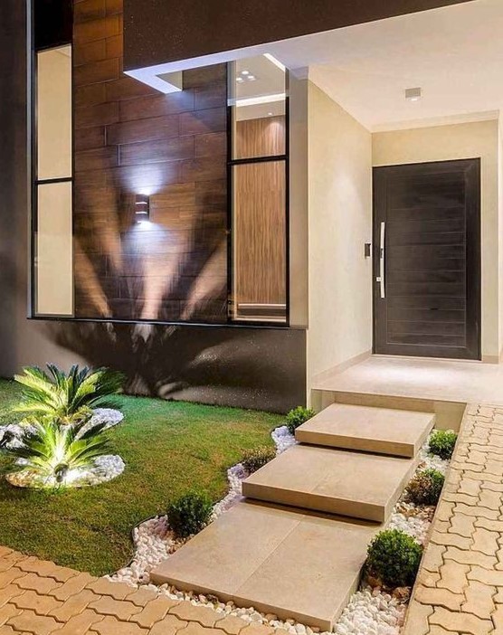an elegant and modern front yard with stone tiles, neutral pebbles, greenery, grass and tropical plants with additional lights