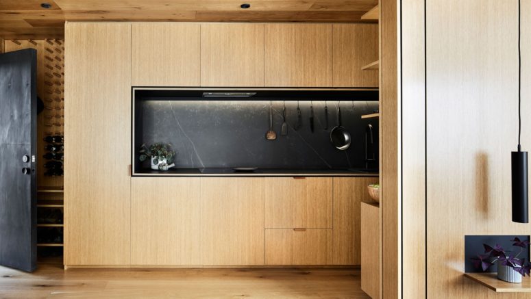wooden cabinets and a black marble backsplash is an awesome mix The kitchen is done with sleek light-colored wood cabinets and a black marble backsplash for a stylish feel