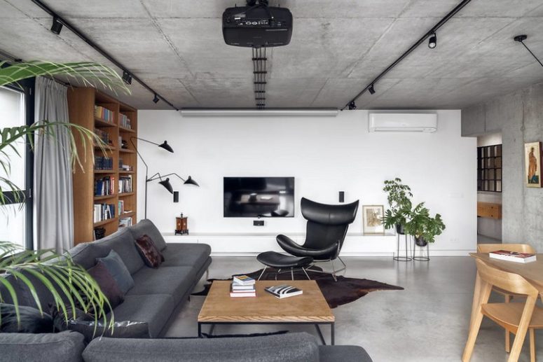 The living room is done wiht a large L shaped sofa, a leather chair with a footrest, a bookcase and some greenery The living room is done wiht a large L-shaped sofa, a leather chair with a footrest, a bookcase and some greenery