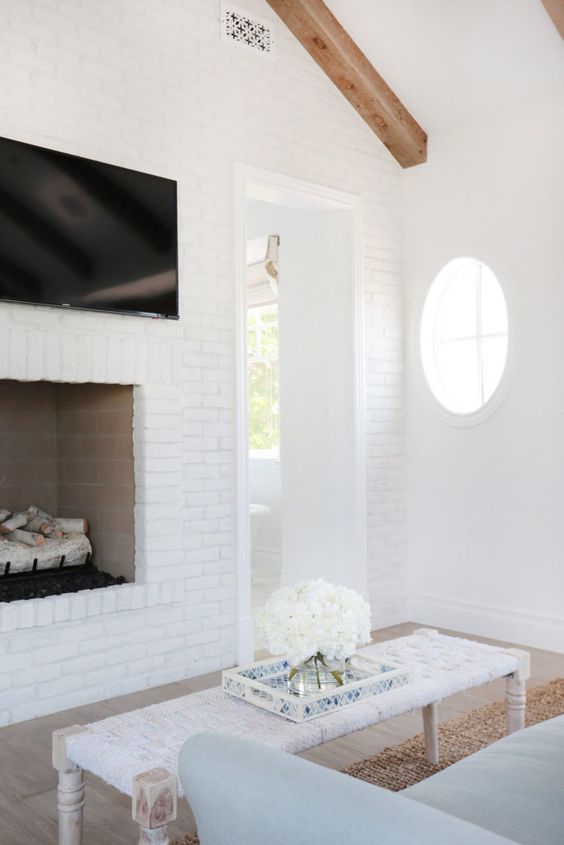 a neutral beach home with white brick walls and a fireplace clad with bricks, a white woven ottoman and a light blue sofa