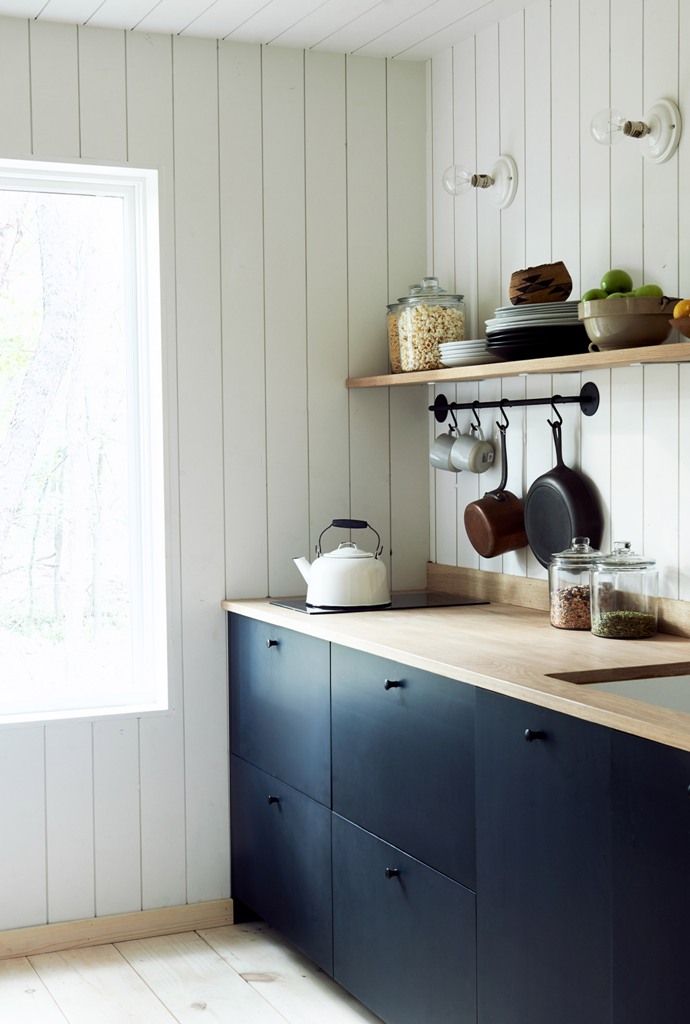The kitchen is done with sleek navy cabinets, light colored wooden shelves and countertops and there's much natural light The kitchen is done with sleek navy cabinets, light-colored wooden shelves and countertops and there's much natural light