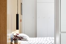 06 The bedroom is small and laconic, it features a woodne headboard that acts as storage, floating nightstandns and pendant lamps