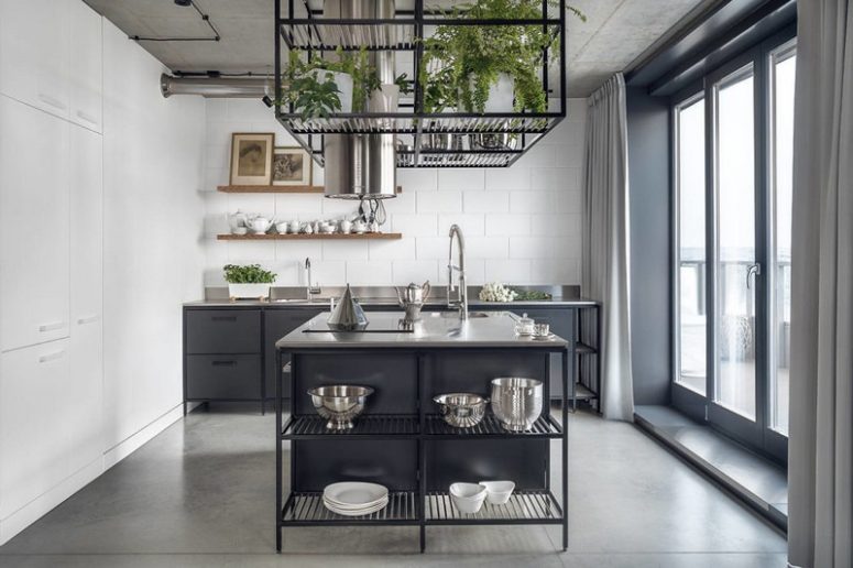 The kitchen is done with black metal cabinets and a kitchen island, with a subway tile wall and a cube with potted greenery