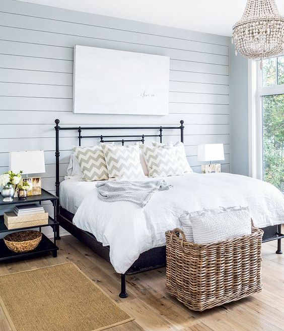 a welcoming farmhouse bedroom with light blue shiplap, a metal bed and a basket for storage