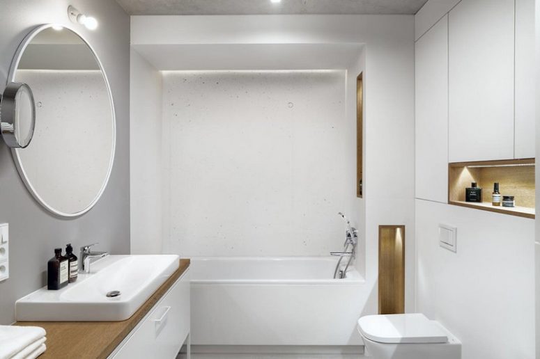 The bathroom is minimal and white, done with sleek surfaces, light wood touches and much storage space