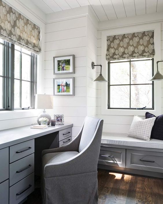 a farmhouse home office done with white shiplap on the walls, comfy blue furniture, printed Roman shades and lamps on the walls