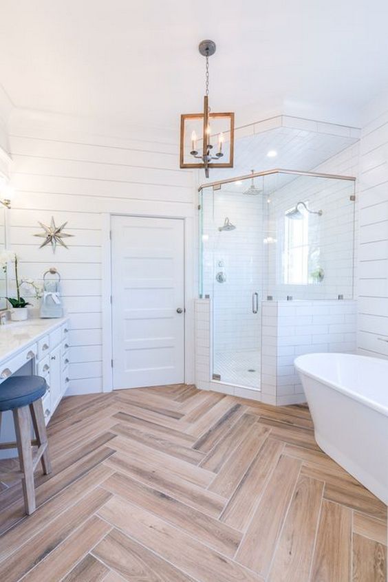 a light-filled farmhouse bathroom featuring white shiplap, a wooden floor, a cool chandelier and a free-standing tub