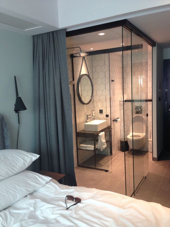 a contemporary bedroom with a small en-suite powder room hidden with glass and curtains