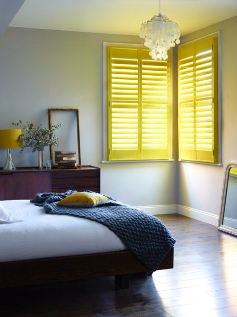 a neutral bedroom with rich-stained furniture and touches of bright yellow - pillows, lamps and shutters