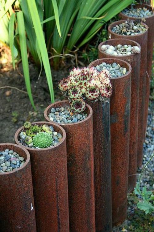 large metal pipes with succulents planted with pebbles in them is a unique and creative idea to border your garden